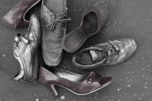 Various abandoned shoes laid on the ground, overhead shot in black and white